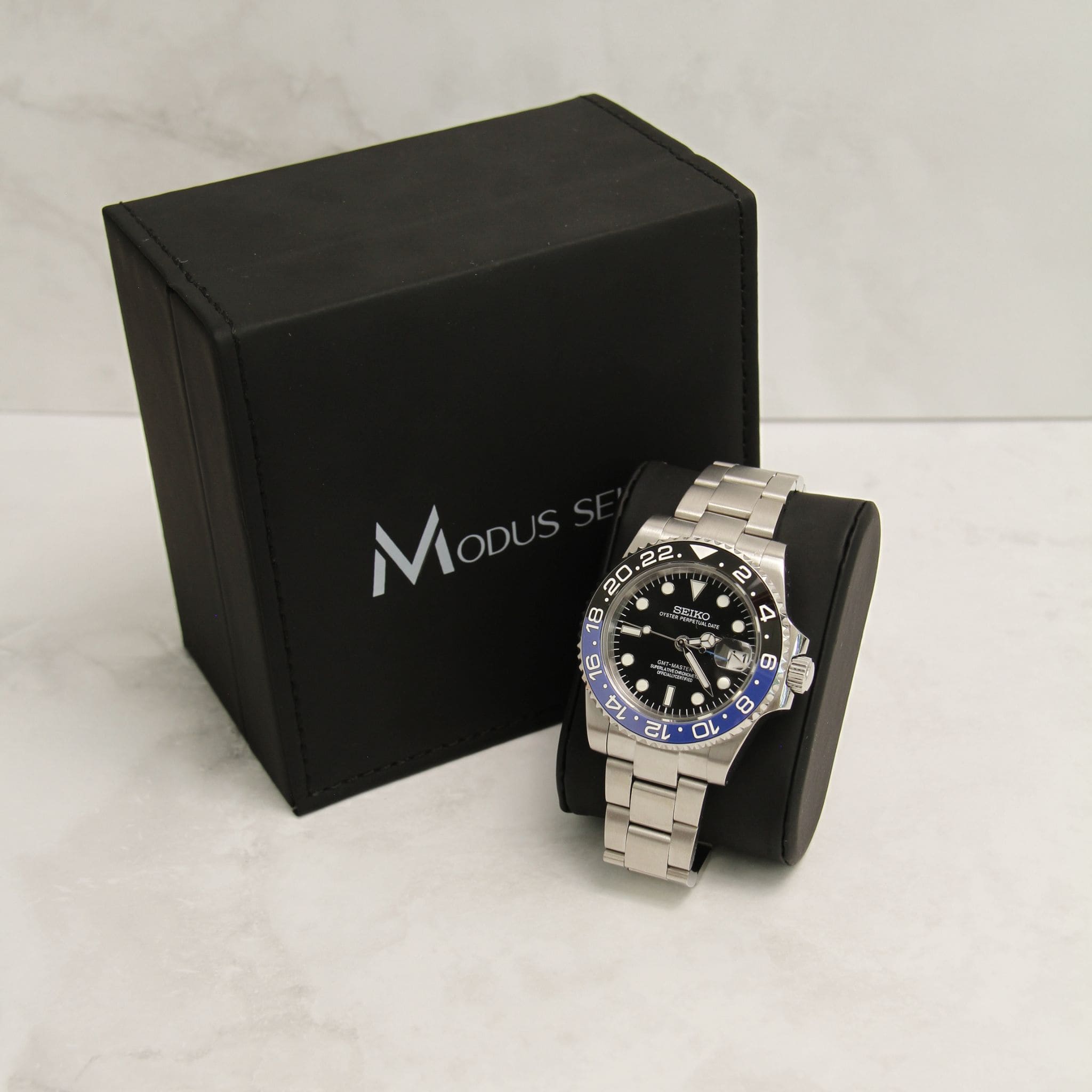 Montre Seiko Mod gmt Batman en gros plan sur coussin noir avec écrin en arrière plan. 